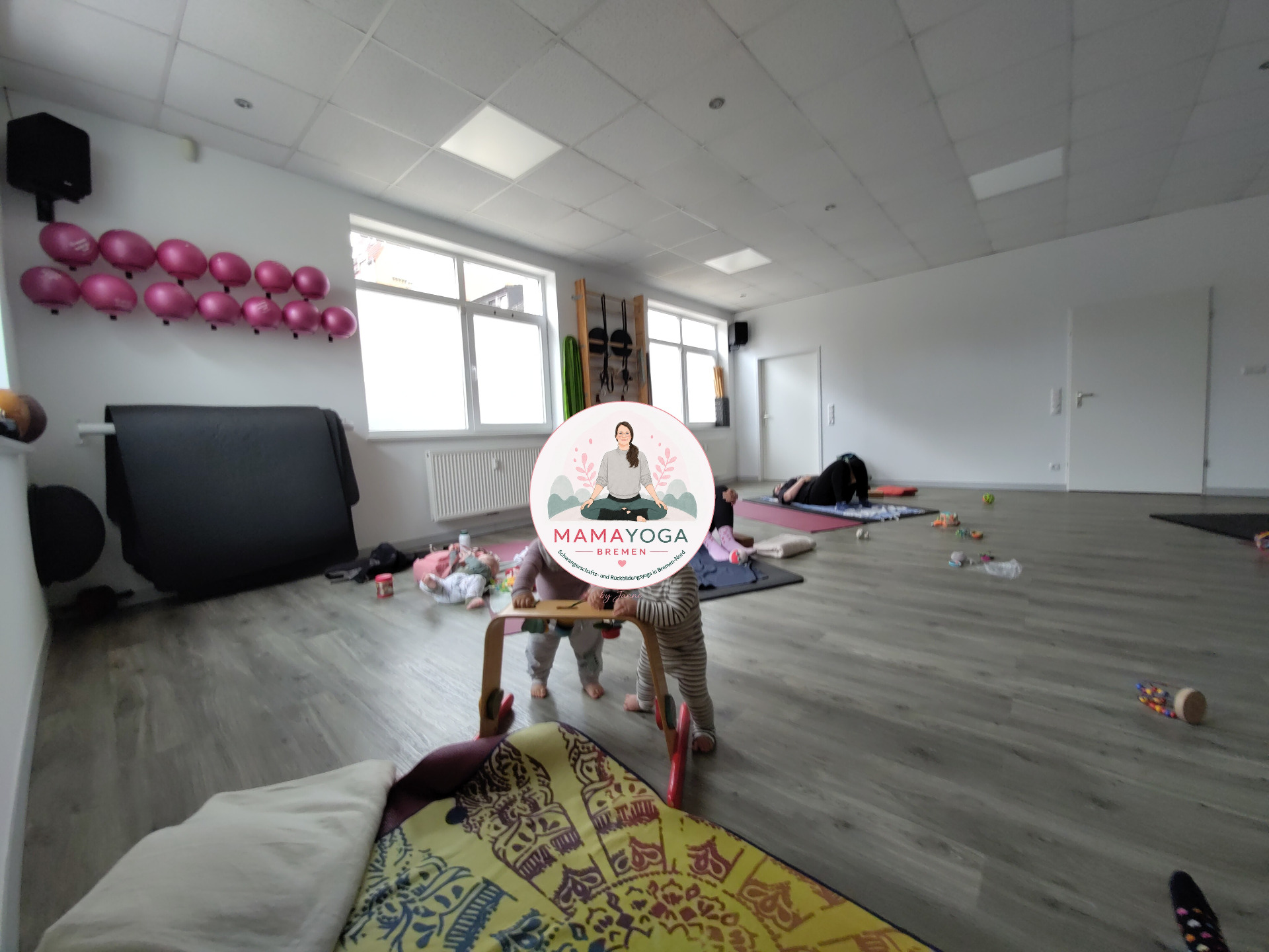 zwei Frauen machen Sonnengrüße im Sitzen und haben ihre Babies im MamaYoga-Kurs dabei.
