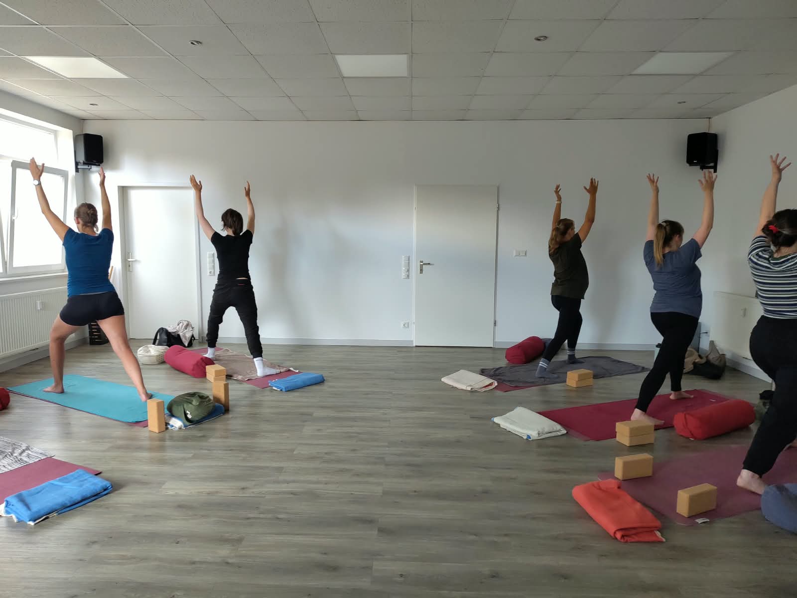 Mehrere Frauen machen Yoga, Kriegen 1, Arme nach oben, auf Matten mit Blöcken und Kissen.